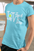 Person wearing a light blue t-shirt with 'LOVE' printed on it, standing outdoors.