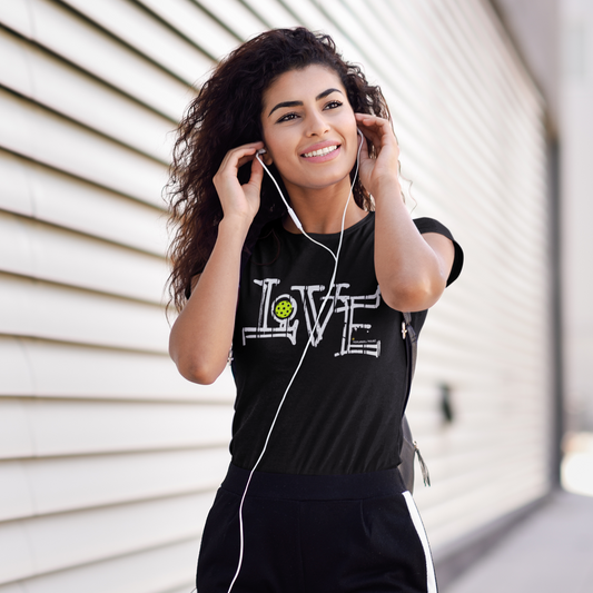 Woman wearing a black 'LOVE' t-shirt with earphones, standing against a light-colored wall.