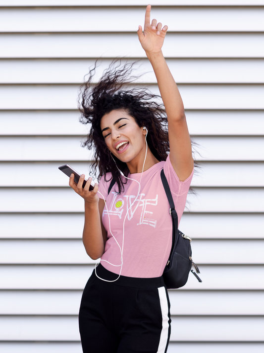 Woman in pink 'LOVE' t-shirt with earphones and phone, against a white wall.