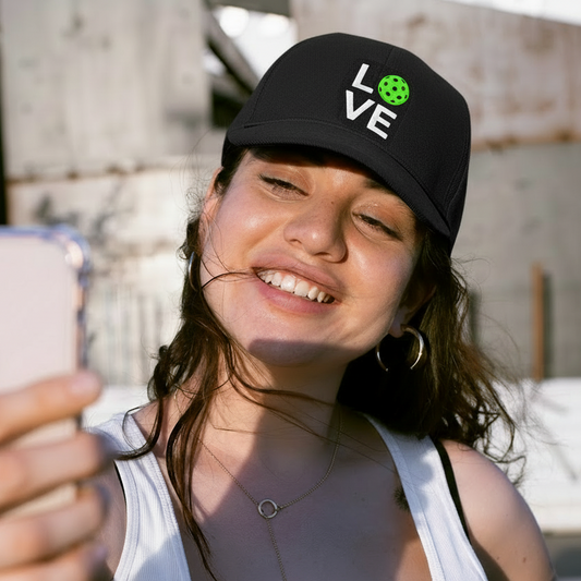 Person taking a selfie wearing a white tank top and black cap with 'LOVE' on it.