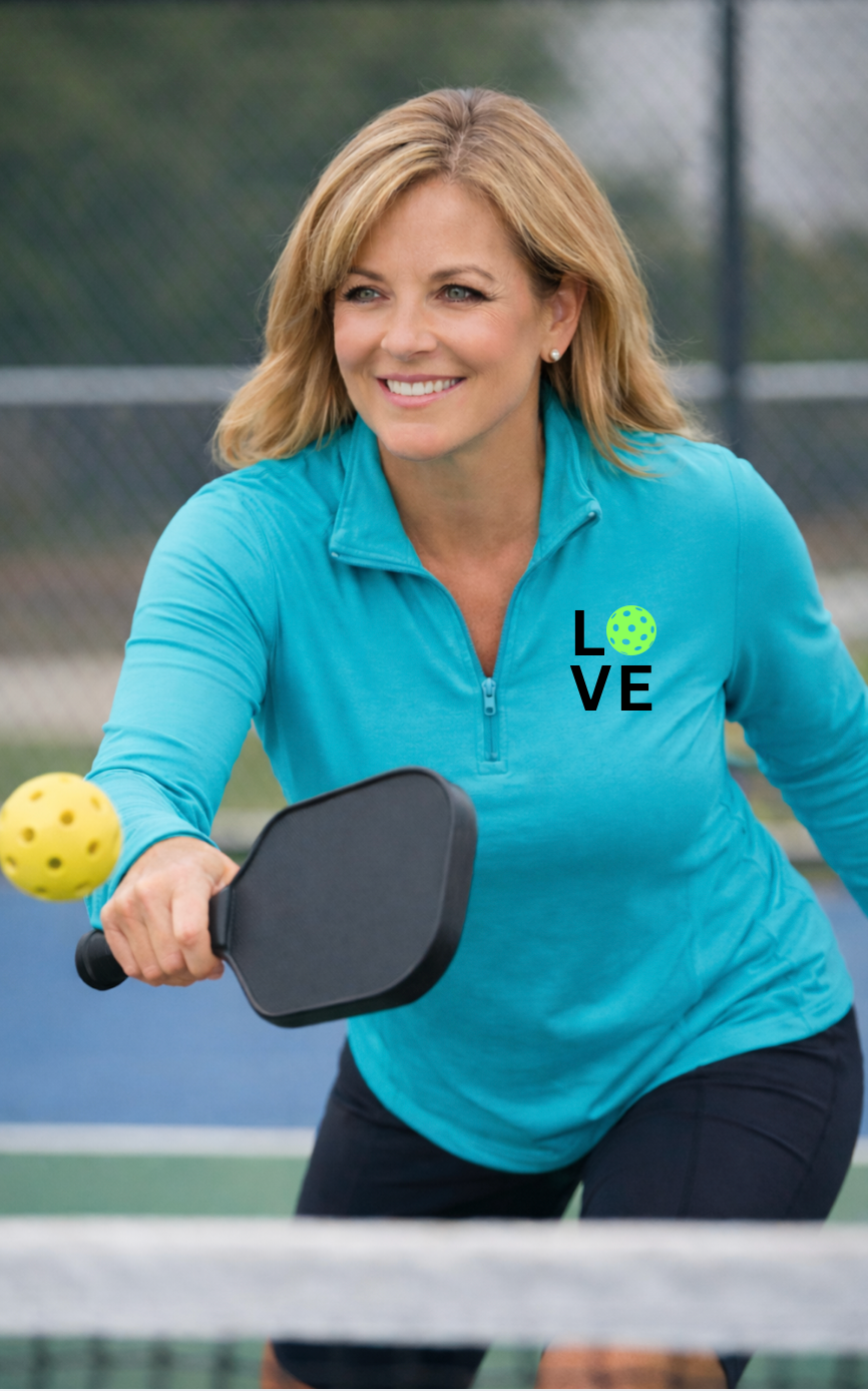 Woman playing pickleball on a court wearing a blue shirt with 'LOVE' printed on it.