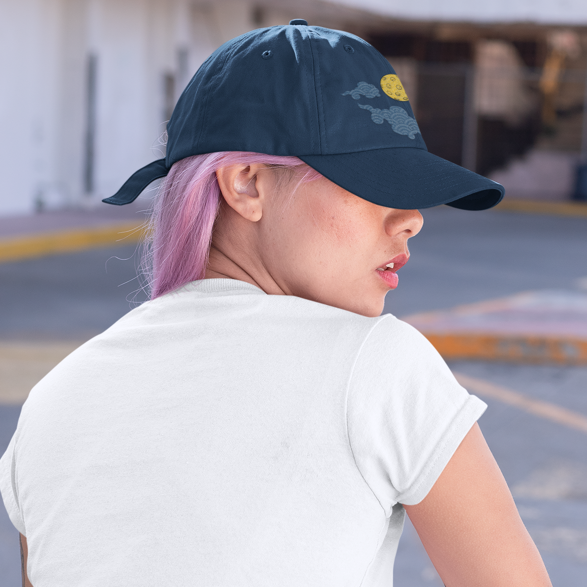 Person wearing a black cap and white t-shirt with pink hair, sitting on a bench.