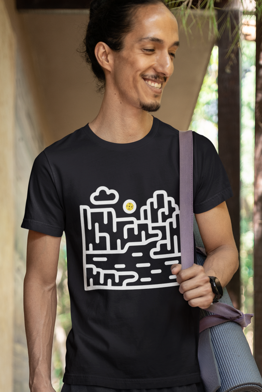 Man wearing a black t-shirt with a white graphic design, standing outdoors near a wooden structure.