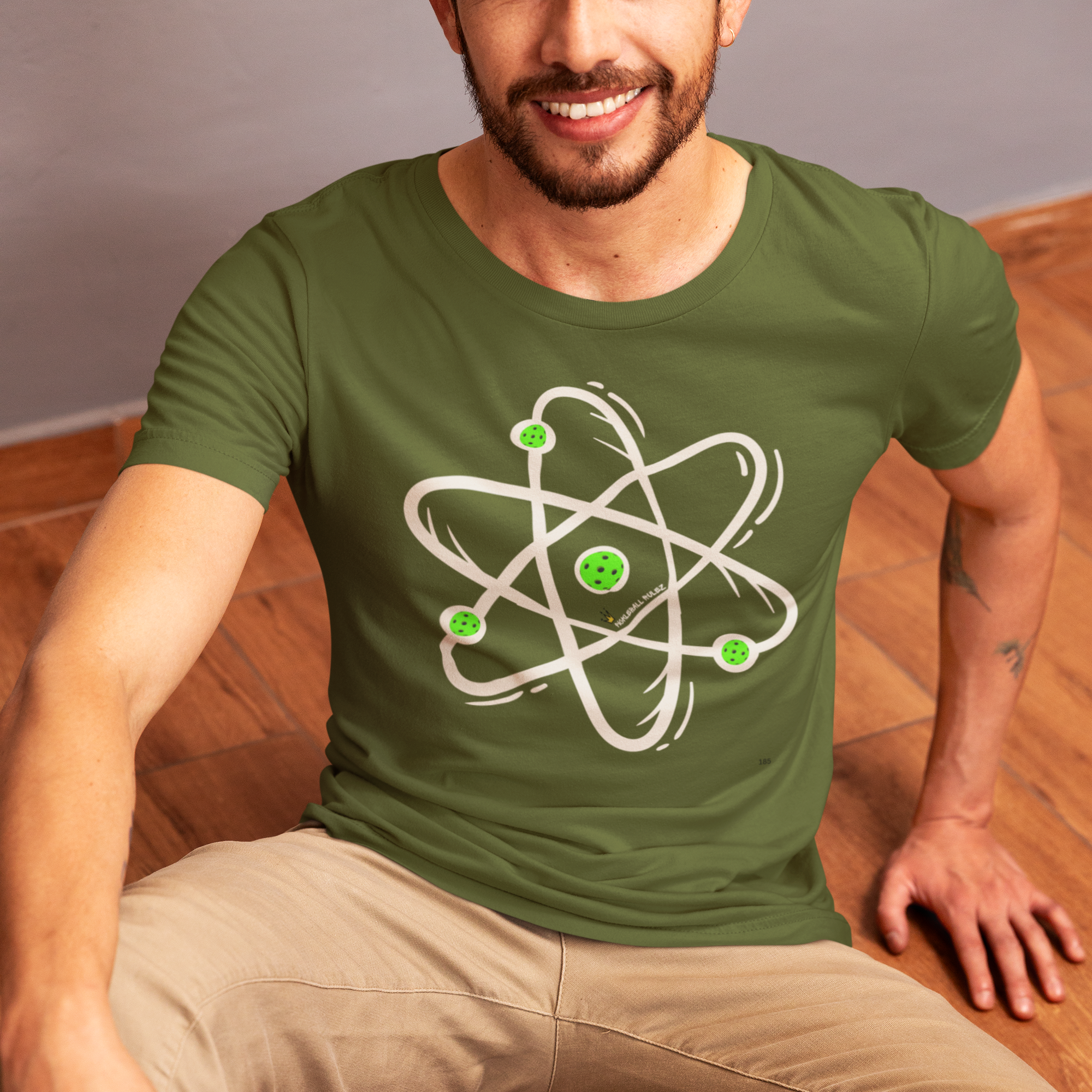 Man wearing a green t-shirt with an atom design sitting on a wooden floor.