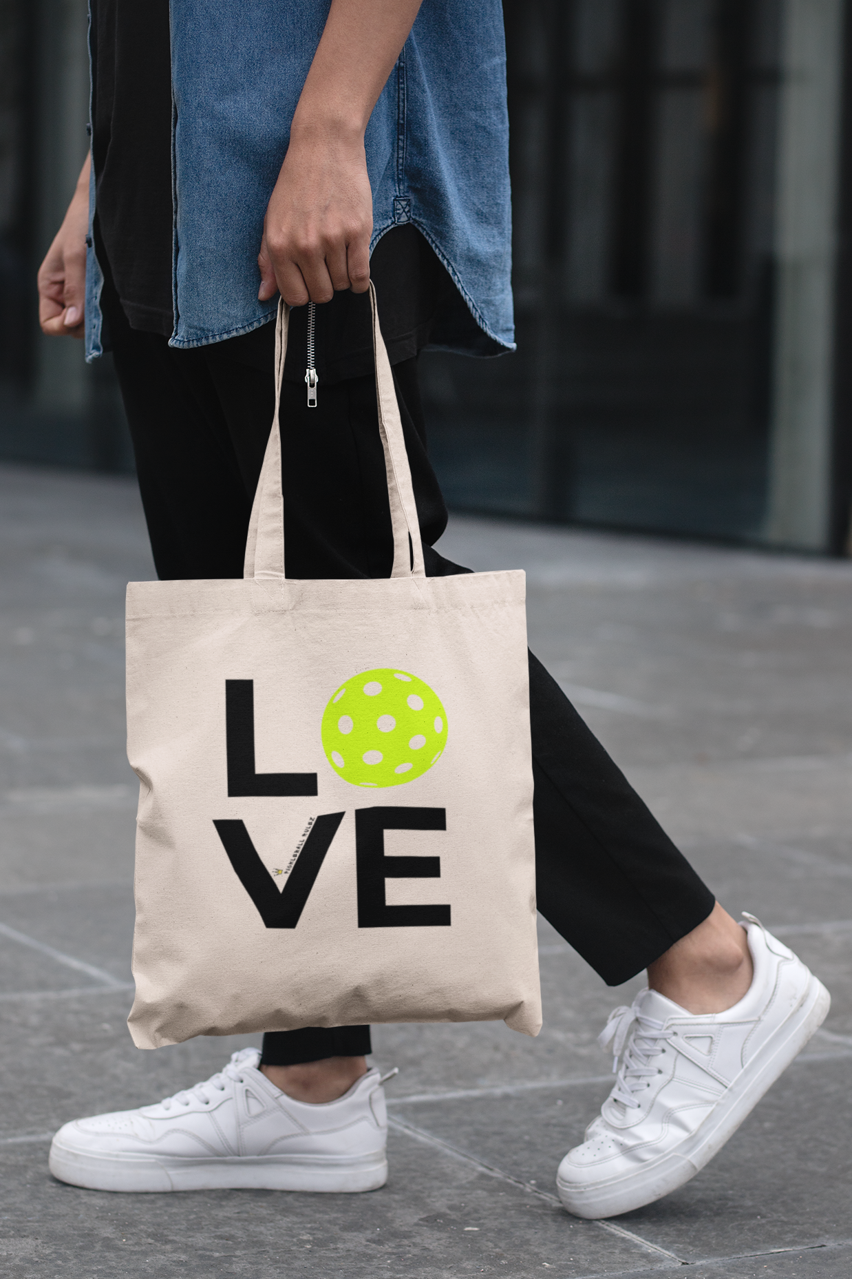 Person holding a tote bag with 'LOVE' printed on it, walking on a pavement.