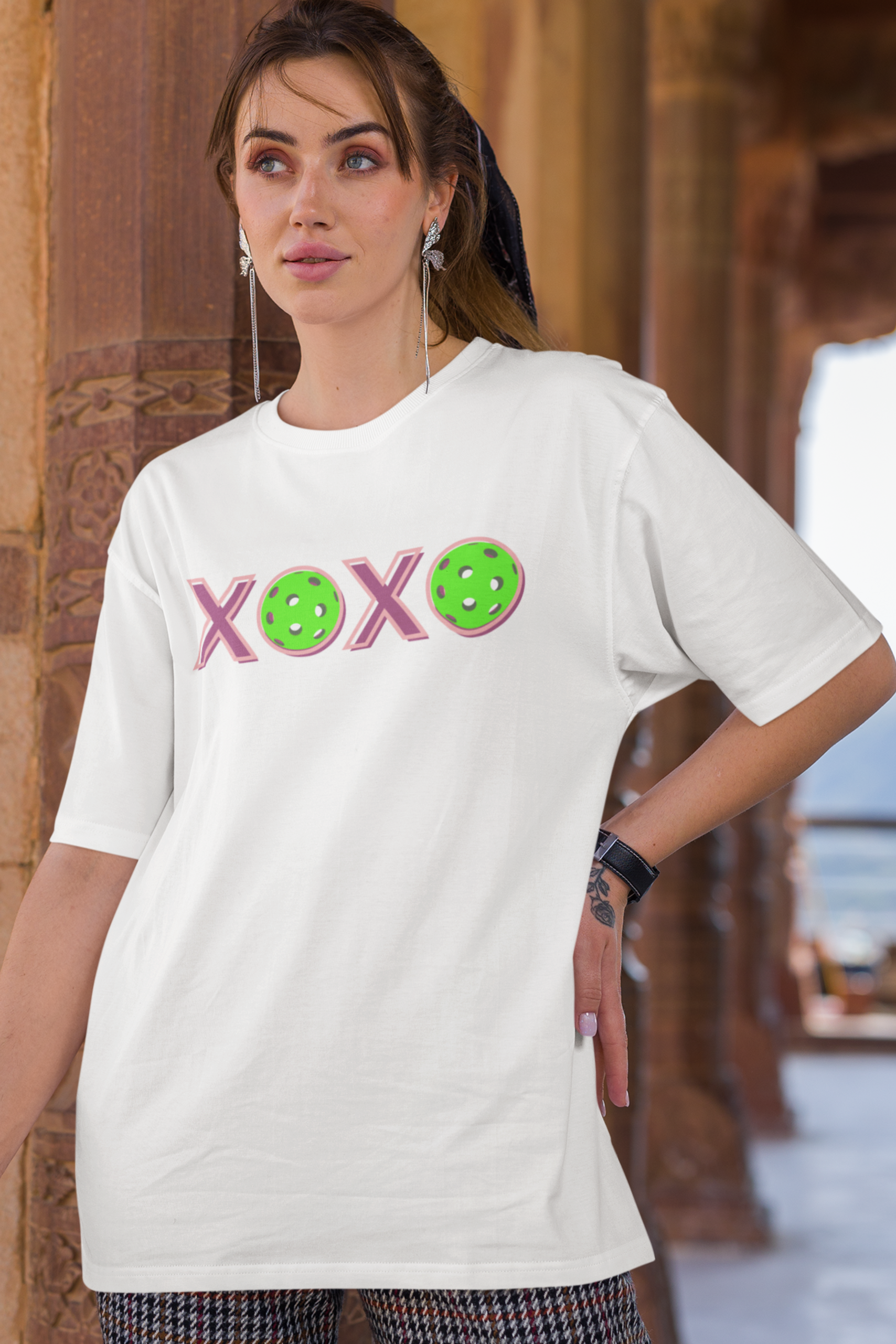 Woman wearing a white t-shirt with colorful text and symbols in an outdoor setting.