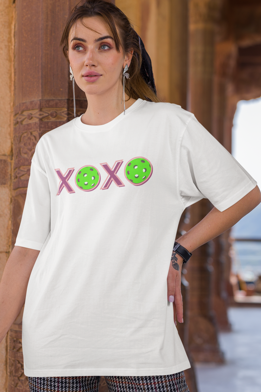 Woman wearing a white t-shirt with colorful text and symbols in an outdoor setting.