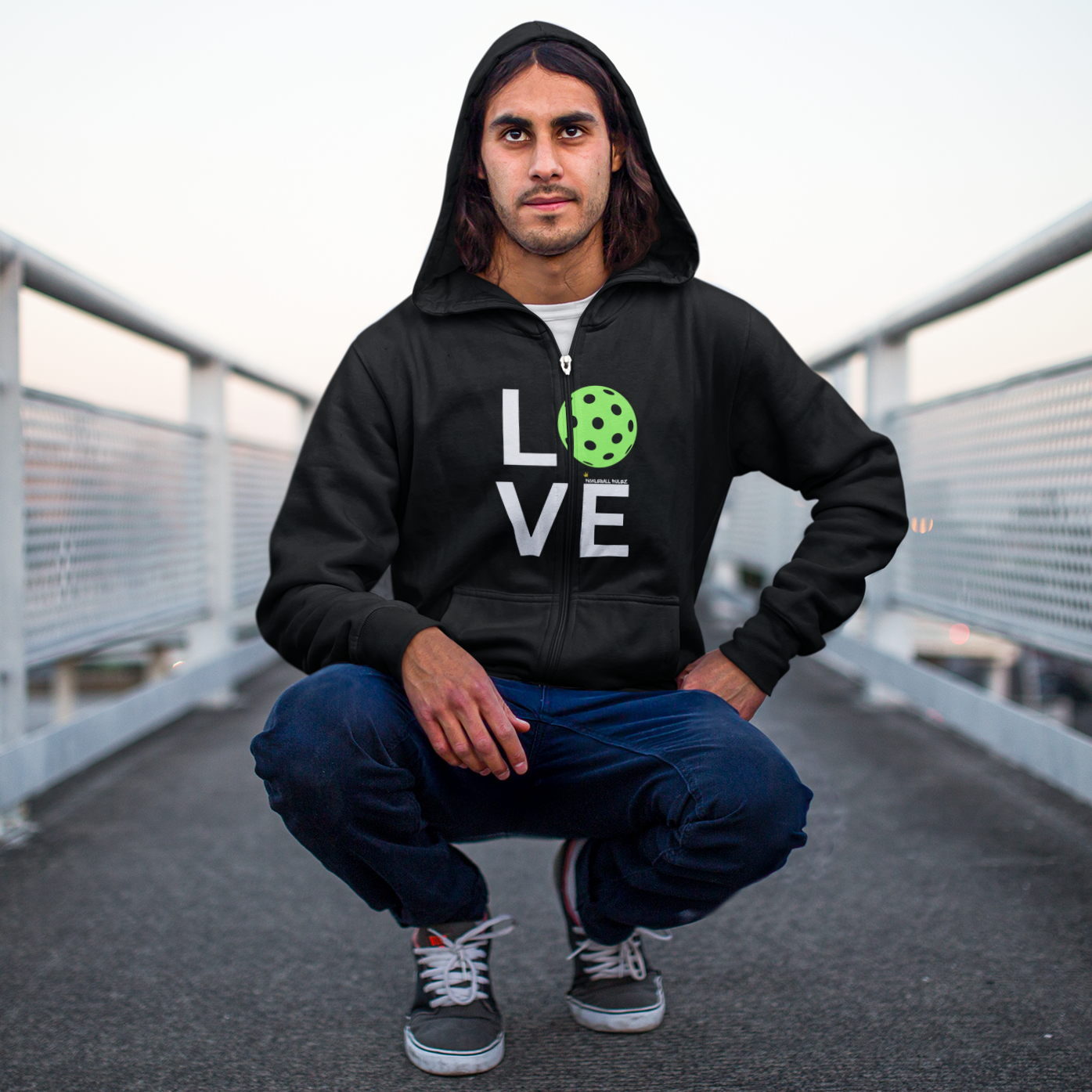 Person wearing a black hoodie with 'LOVE' printed on it, squatting on a bridge.