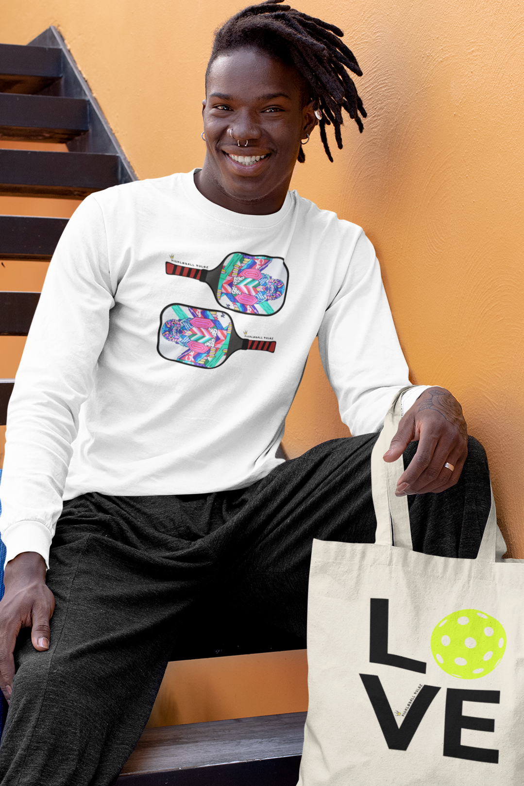 Person wearing a white sweatshirt with pickleball designs, holding a tote bag with 'LOVE' and a pickleball graphic.