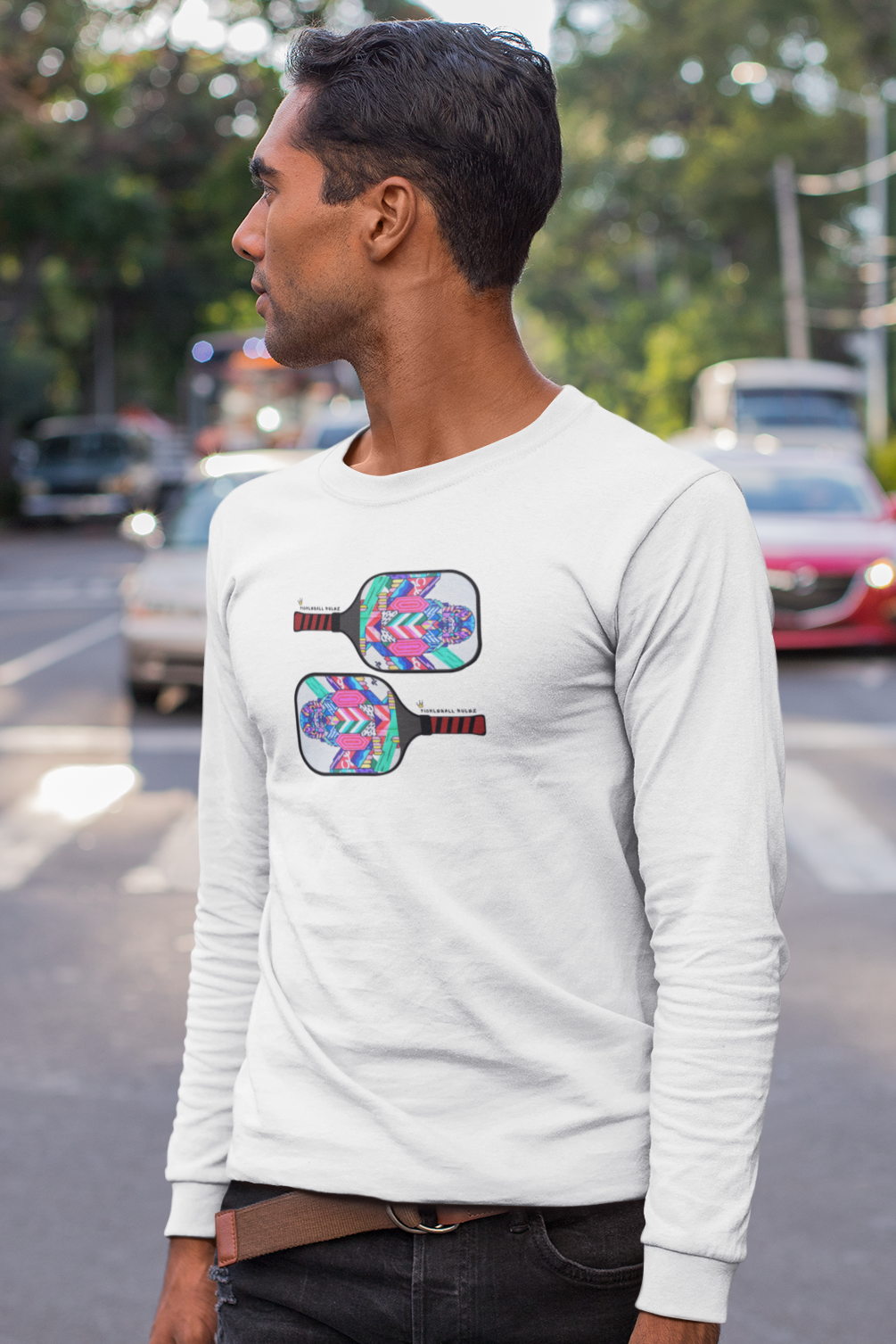 Man wearing a white long-sleeve shirt with pickleball paddle design on a street.