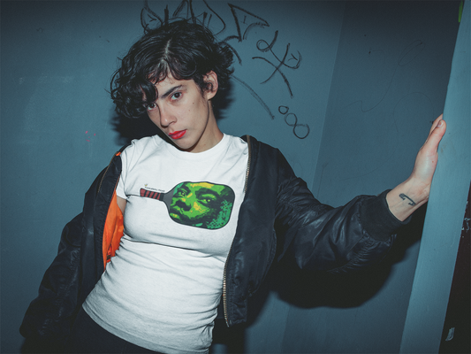 Person wearing a white t-shirt with a graphic design, standing against a blue wall with graffiti.