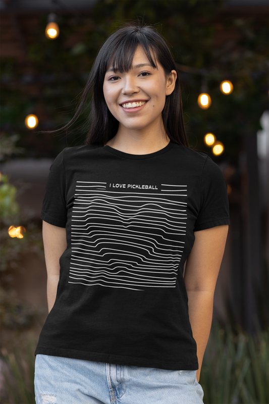 Woman wearing a black t-shirt with 'I love pickleball' design, standing outdoors with string lights in the background.