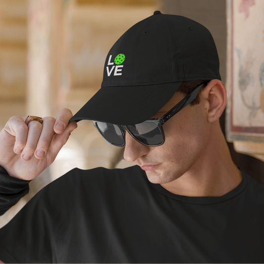 Man wearing a black cap with 'LOVE' printed on it, sunglasses, and black wristband indoors.