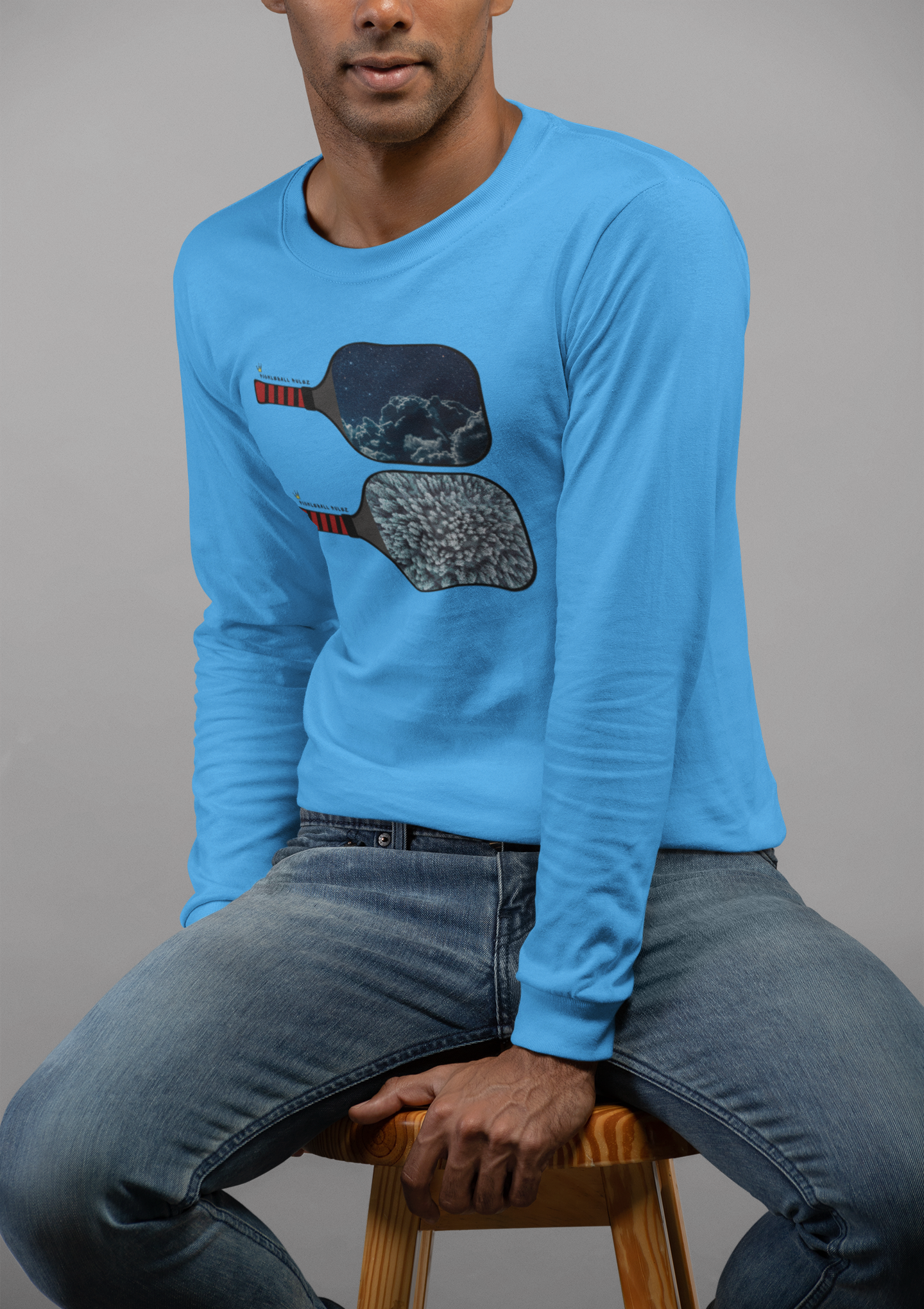 Person wearing a blue sweatshirt with graphic design sitting on a stool against a gray background