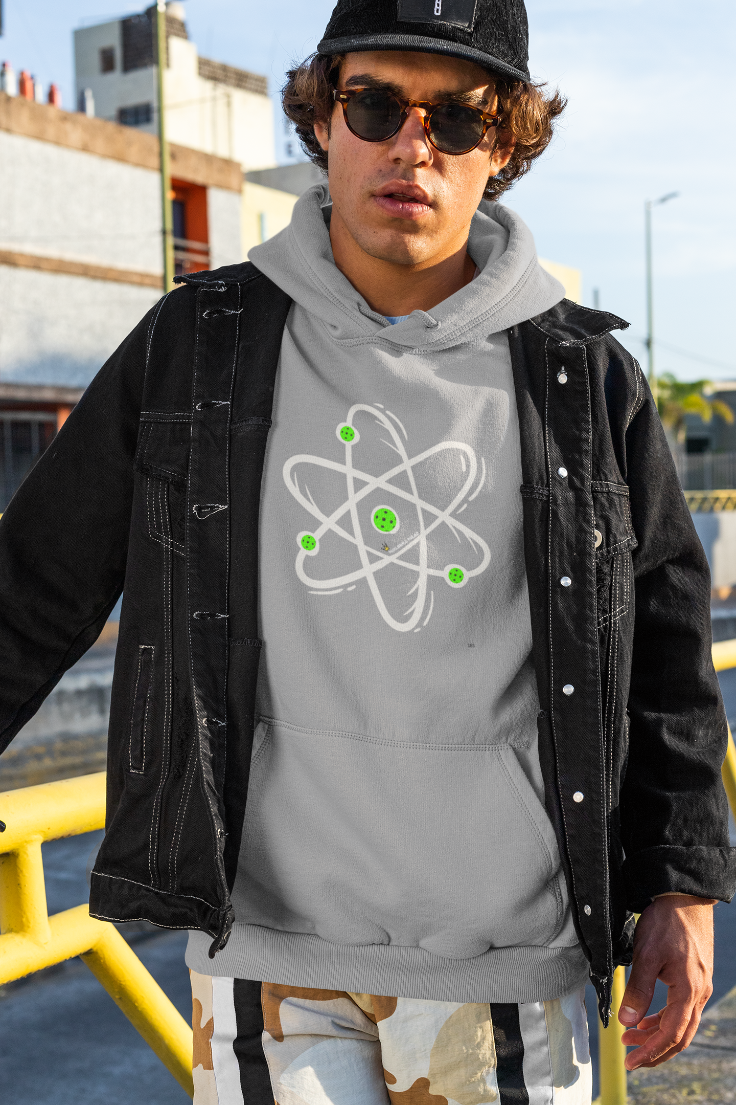 Person wearing a gray hoodie with an atom design, black jacket, and sunglasses outdoors.
