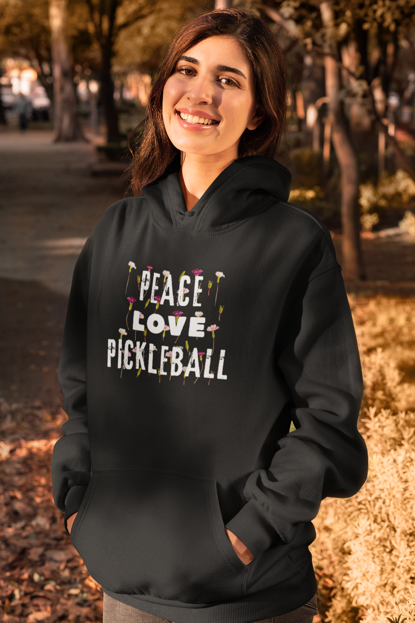 Woman wearing a black hoodie with 'Peace Love Pickleball' text outdoors.