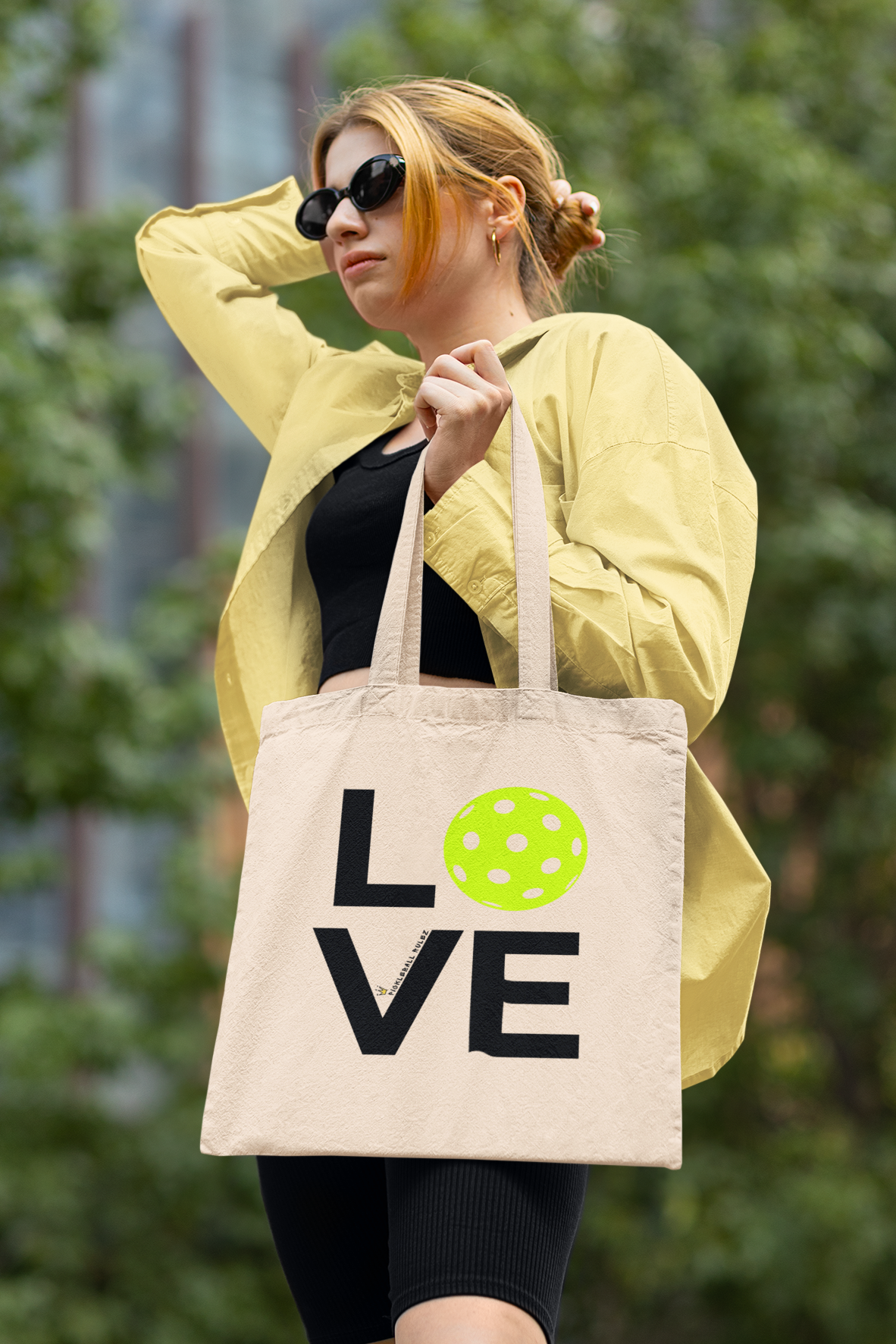 Woman holding a tote bag with 'LOVE' and a green heart design outdoors.