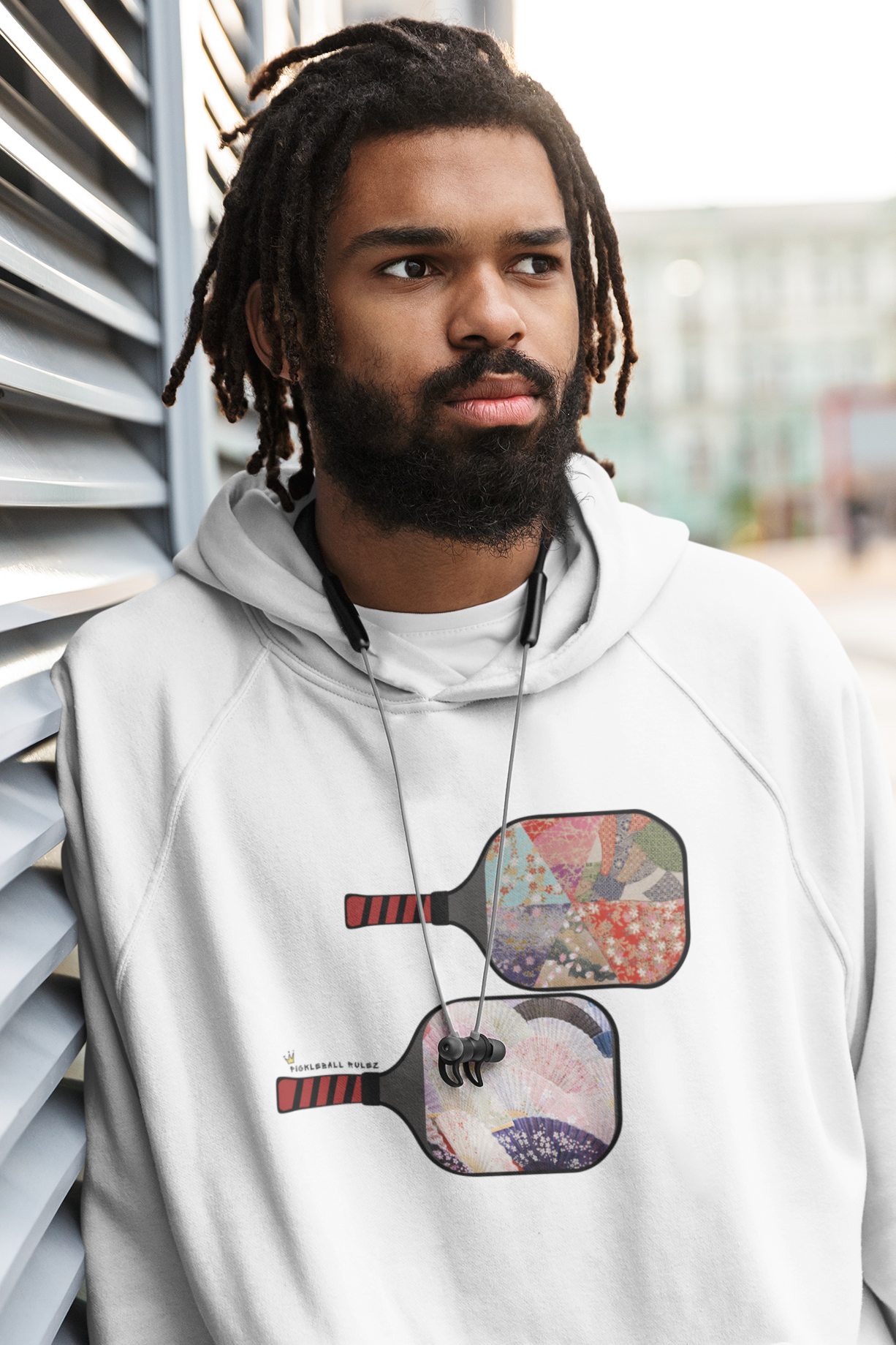 Man wearing a white hoodie with graphic design, standing against a modern building.