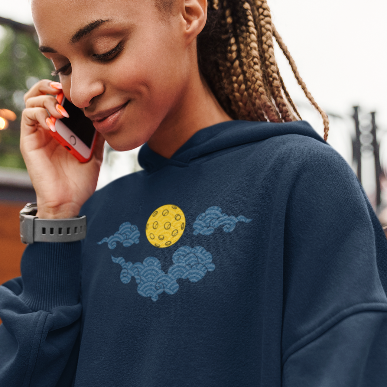 Woman wearing a navy hoodie with a cloud and moon design, talking on a red phone.