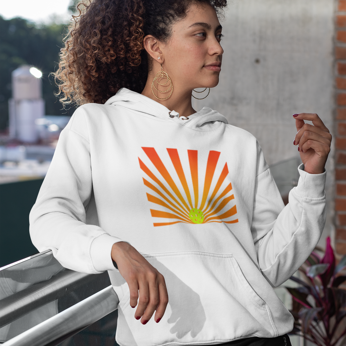 Woman wearing a white hoodie with a colorful sun graphic, standing outdoors.
