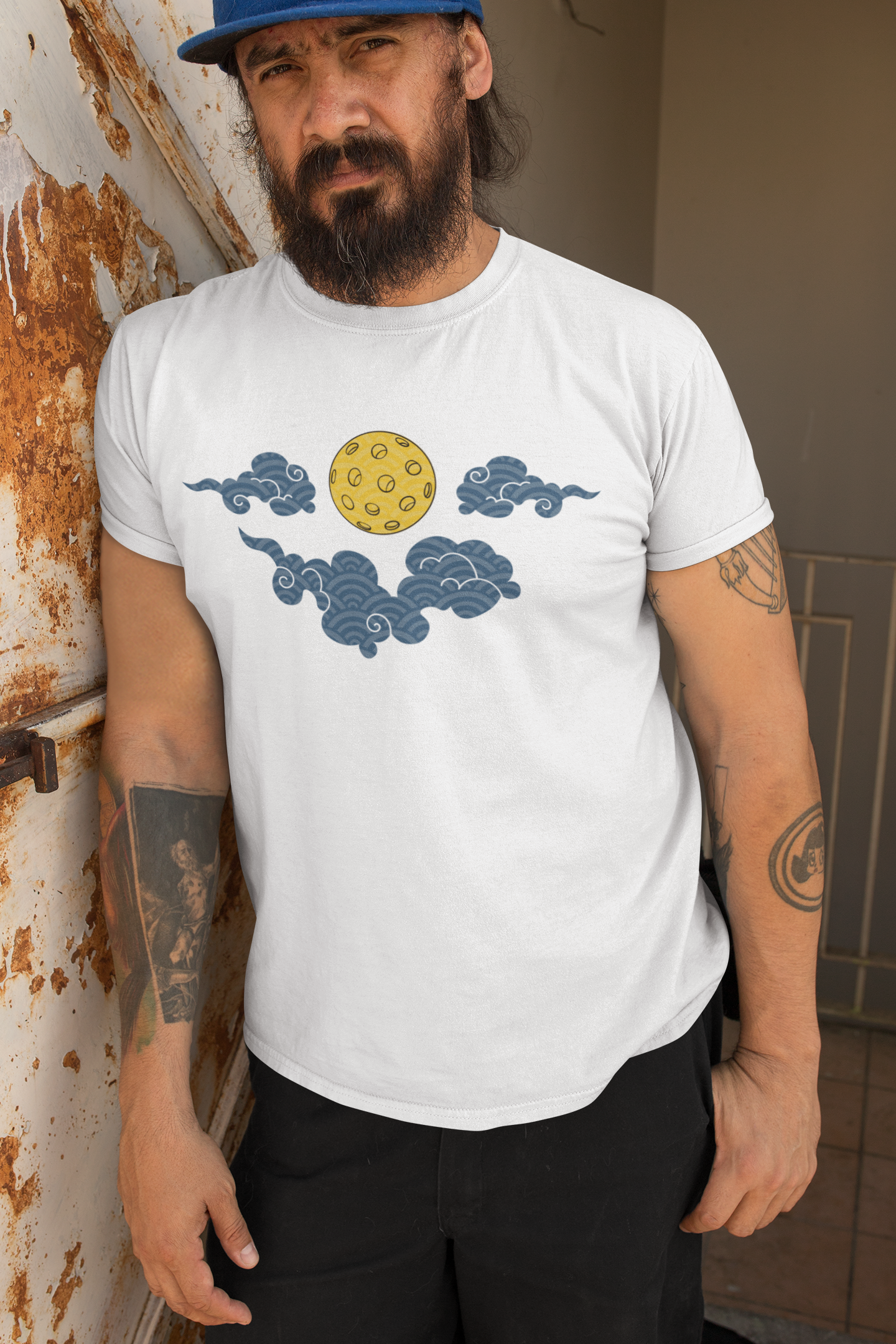 Man wearing a white t-shirt with cloud and sun design, standing against a rusty metal wall.