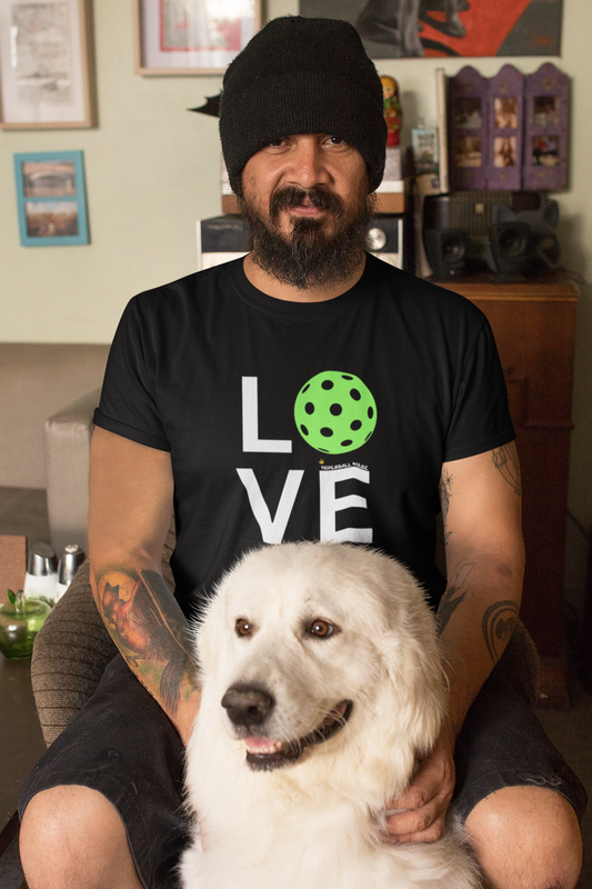 Man wearing a black t-shirt with a dog graphic and text, sitting with a white dog in a room.