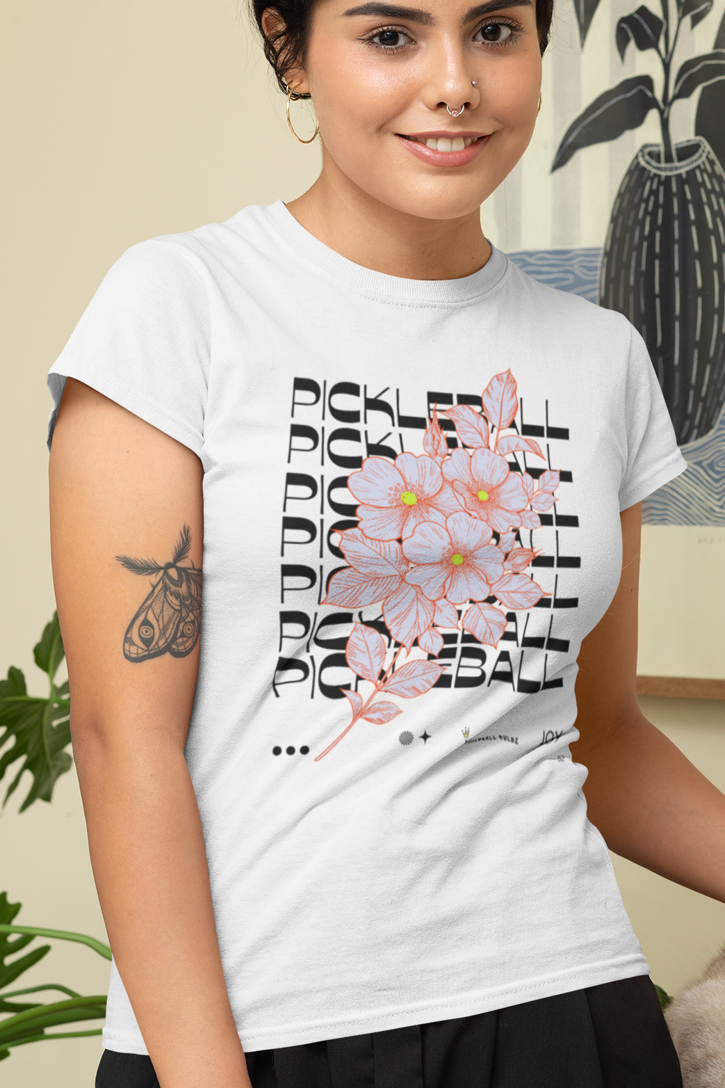 Woman wearing a white t-shirt with floral design and text, standing indoors with a cat.