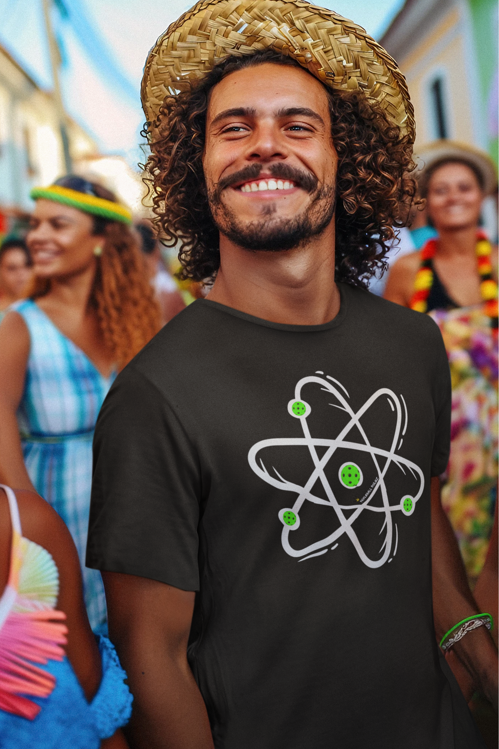 Man wearing a straw hat and black t-shirt with a graphic design, standing in a colorful outdoor setting.