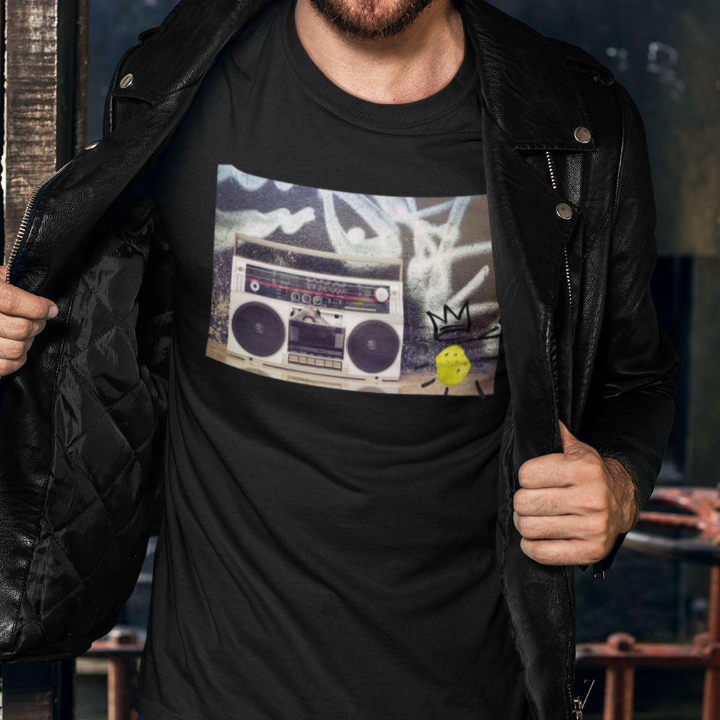 Man wearing a black t-shirt with a graphic design, standing in front of a graffiti-covered wall.
