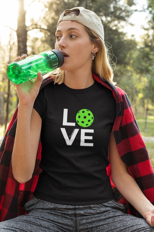Woman sitting outdoors drinking from a green bottle, wearing a black t-shirt with 'LOVE' and a green heart.