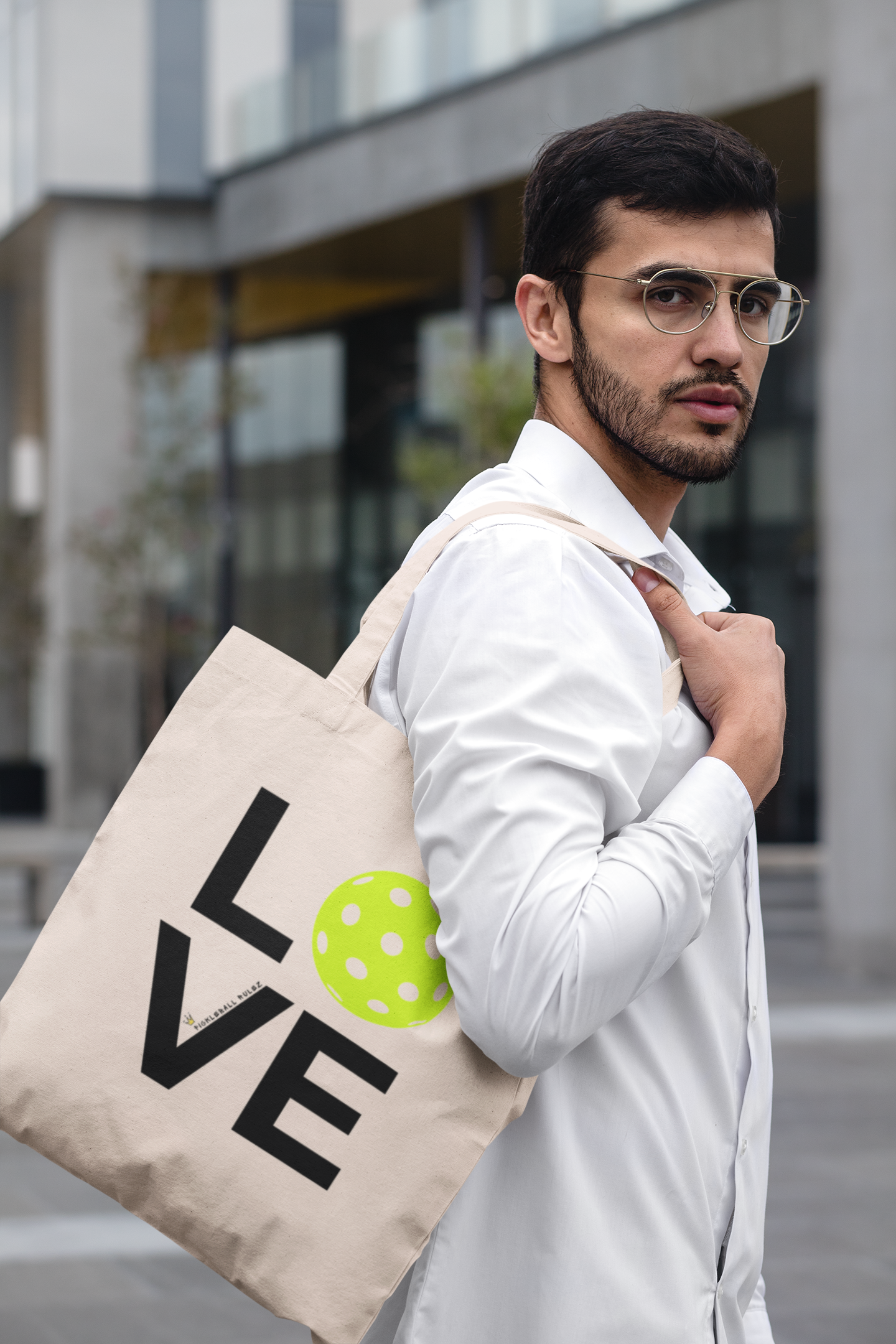 Man wearing glasses and a white shirt, holding a beige tote bag with 'LOVE' printed on it.