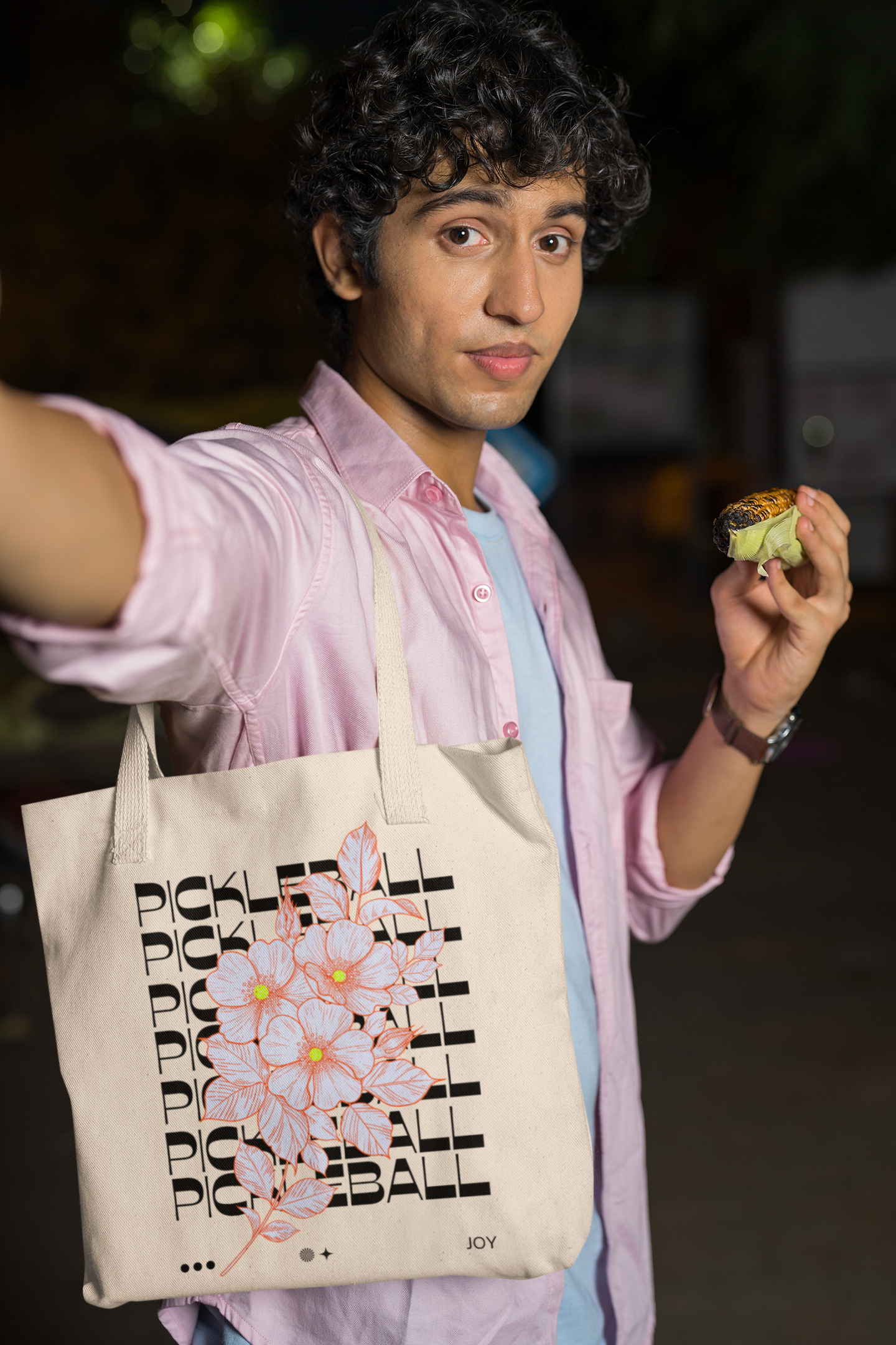 Person holding a tote bag with text and a flower design, outdoors at night.
