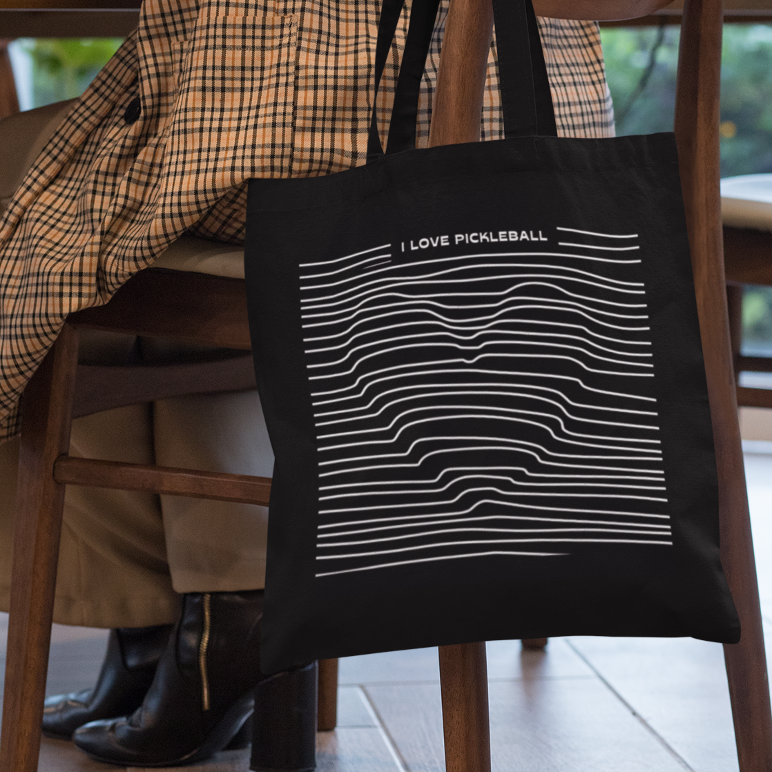 Person sitting at a table with a black tote bag featuring white graphics and text.