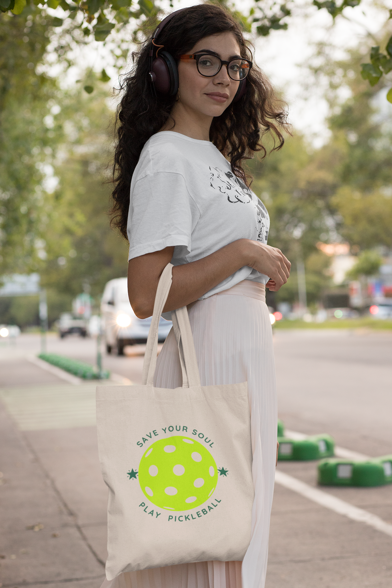 Woman holding a tote bag with a pickleball design on a sidewalk.